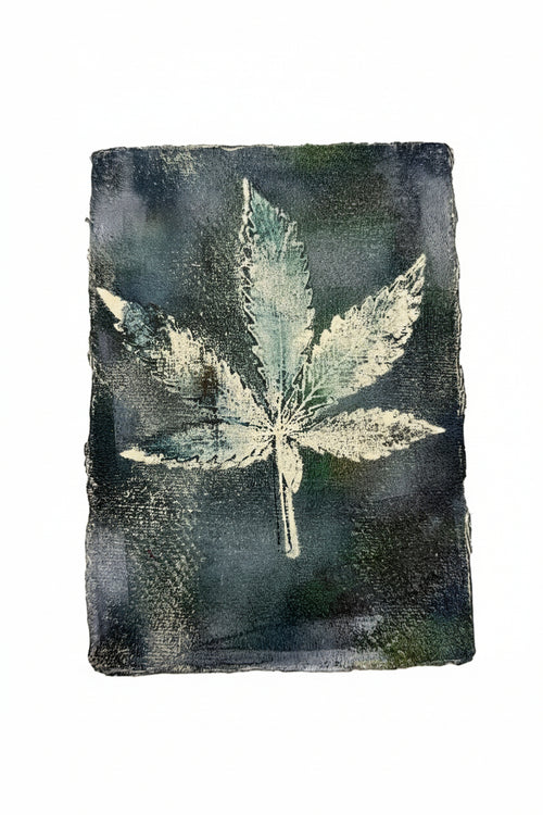 A square dark charcoal or black ink print featuring a light-colored leaf design, displayed against a plain off-white background.
